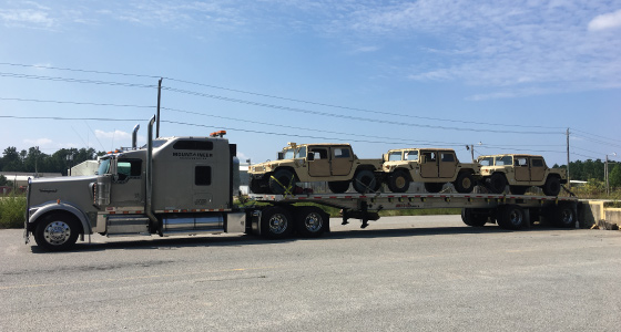 Flatbed carrier truck carrying three high mobility multipurpose wheeled vehicles Flatbed carrier truck carrying three high mobility multipurpose wheeled vehicles